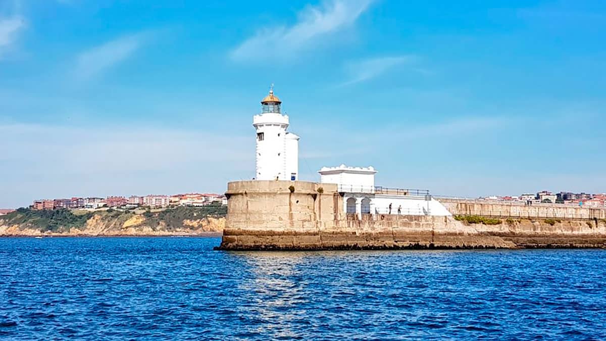 Vista del faro blanco, el espigón que da acceso y el mar rodeándolo